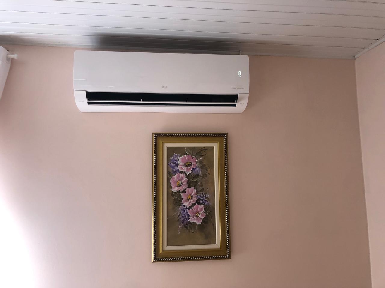 aparelho de ar-condicionado LG branco instalado em parede bege com um quadro de flores emoldurado abaixo dele