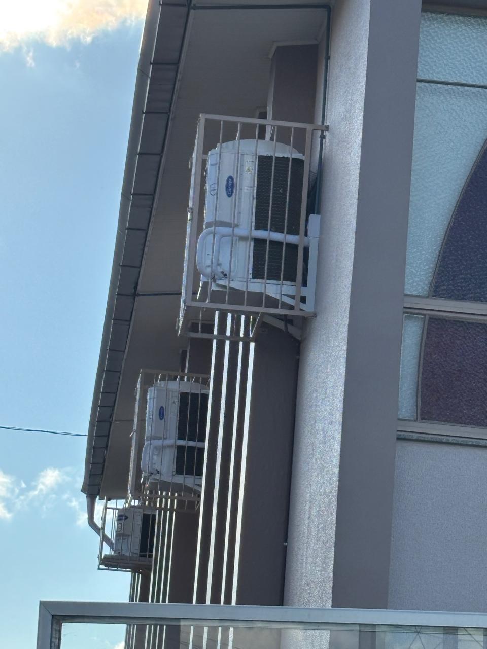 Unidades externas de ar-condicionado Carrier instaladas na fachada de um prédio, protegidas por gaiolas metálicas branca