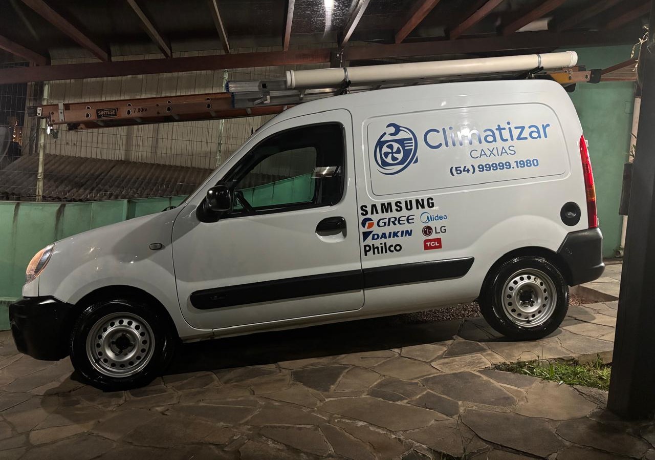 van branca da empresa Climatizar Caxias com adesivos de marcas de ar-condicionado, estacionada sob uma cobertu